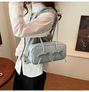 Sac Boston en cuir verni bleu clair avec double nœuds porté par un modèle
