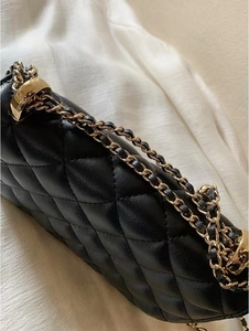 Détail de la texture matelassée noire et de la bandoulière chaîne dorée du sac à main