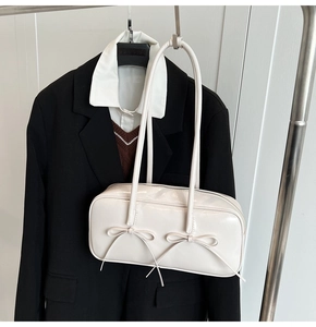 Détail d'un sac Boston blanc crème brillant avec des nœuds élégants sur un porte-manteau