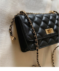 Détail d'un sac bandoulière matelassé noir avec fermoir doré rotatif et bandoulière chaîne