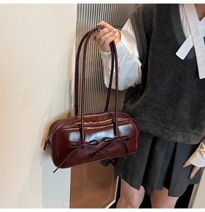 Détail d'un sac à bandoulière bordeaux foncé avec nœuds et finition en cuir verni brillant