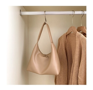 Detail der beigen halbmondförmigen Tasche an einem Kleiderhaken im Kleiderschrank