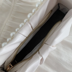 Detail of a beige cloud bag showing the metal zipper and pearl handle craftsmanship