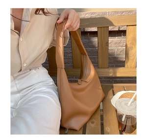 Detail der karamellbraunen Hobo-Tasche aus Leder mit breitem Gurt auf einer Holzbank