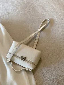 Detail der elfenbeinweißen quadratischen Handtasche mit Litschistruktur und Metallreißverschluss