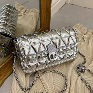 Silver quilted crossbody bag with metal chain strap and twist lock on a beige backdrop