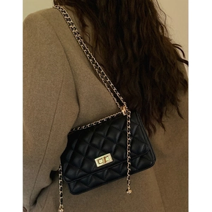Sac bandoulière matelassé noir élégant avec chaîne dorée porté par une femme en blazer brun