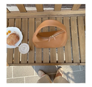 Draufsicht einer braunen Leder-Halbmond-Tasche auf einer Holzbank bei Sonnenlicht