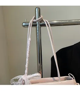 Close-up of pink shoulder bag featuring a unique strap with white lace ribbon detail