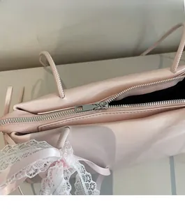 Detail view of pink leather bag featuring silver metal zipper and lace ribbon bow decoration