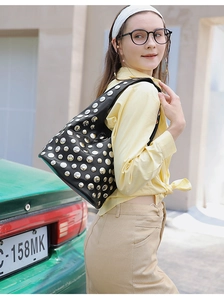 Detail of black leather shoulder bag with silver star rivets shown in street style scene