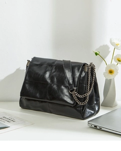Close-up of black glossy leather bag with block stitching and vintage chain strap