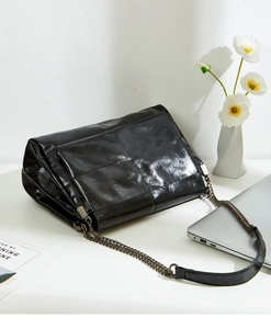 Detailed close-up of glossy black quilted leather handbag with bronze metal chain strap