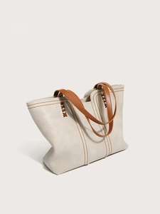 Close-up of contrast stitching and leather texture on a beige tote bag with brown straps
