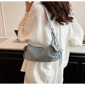 Detail of light blue denim shoulder bag featuring side drawstring flap pockets for women