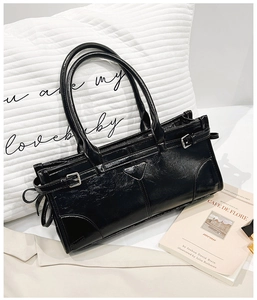Nahaufnahme der schwarzen glänzenden Ledertasche mit Knitteroptik und seitlichen Metallschnallen