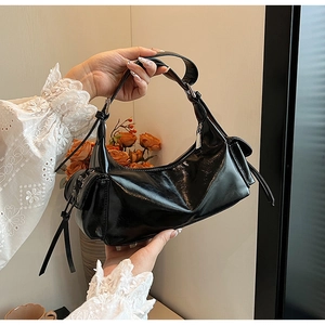 Close-up of black glossy leather shoulder bag with decorative side lace-up pocket detail