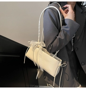 Close-up of a white patent leather baguette bag featuring elegant lace bow detailing