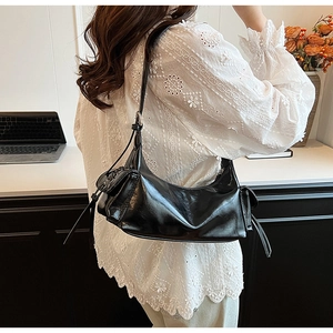 Detail of black glossy leather shoulder bag featuring a side flap pocket and long tassels