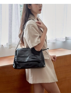 Close-up of a black leather shoulder bag with a silver chain strap in a minimal setting