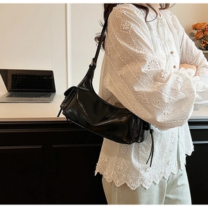 Detail of a black glossy leather shoulder bag featuring a stylish leather fringe pendant