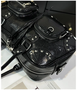 Macro shot of glossy black patent leather with silver studs and zipper detail on hand bag
