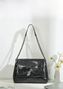 Detail of glossy black chain crossbody bag with square quilted stitching and metal strap