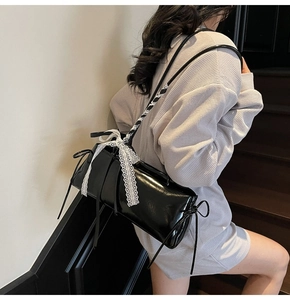 Close-up of black glossy shoulder bag with white lace bows and Balletcore details
