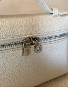 Detail der weißen Tasche aus genarbtem Leder mit Doppelreißverschluss und Goldanhänger