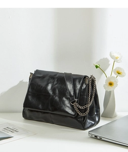 Detail of black quilted leather shoulder bag with silver chain strap on white desk