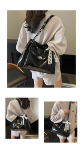 Detail of glossy black tote bag with white lace bow and silver metal twist lock