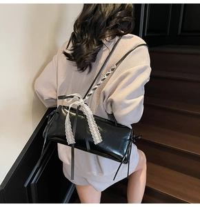 Detail of black glossy baguette bag with white lace bow accents on slim shoulder straps