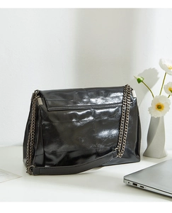 Close-up of a glossy black leather shoulder bag with a metal chain and leather strap