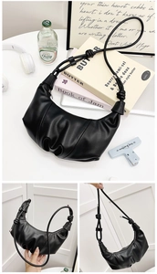 Close-up of black croissant bag with cloud pleats and knotted strap on a white table