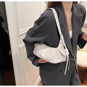 Close-up of white leather underarm bag featuring decorative woven ties on a gray blazer