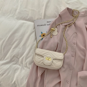 Detail of cream quilted crossbody bag featuring V-shaped texture and gold hardware