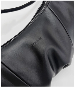 Close-up of black pleated leather croissant bag with FASHION embossed detail and silver zipper