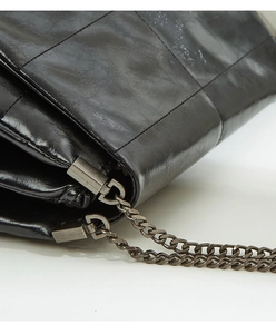 Detail of black quilted leather texture and vintage metal chain hardware on shoulder bag