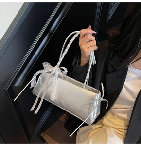 Detail of silver balletcore baguette bag featuring white lace trim and delicate ribbon bows