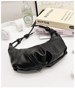Detail of black pleated croissant bag with knotted strap and minimalist synthetic leather