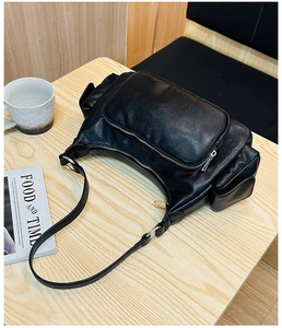 Close-up of black leather multi-pocket shoulder bag on a wooden table with accessories