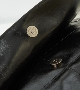 Macro detail of glossy black leather tote with silver magnetic buckle and textured grain