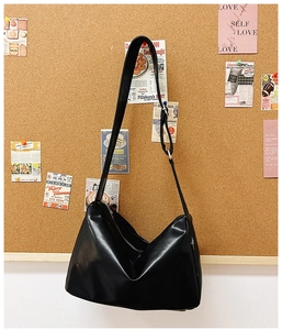 Detail of black faux leather hobo bag with adjustable wide strap on a cork background