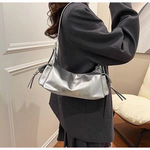 Detail of silver metallic leather shoulder bag with side tassels on a model in a grey blazer