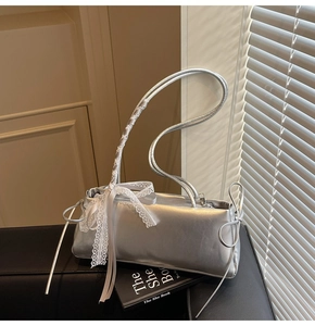 Close-up of silver shoulder bag with delicate white lace bows and drawstring detail