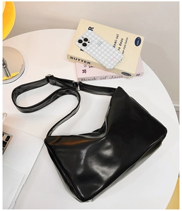Detail view of a large black minimalist hobo bag made of smooth faux leather on a table
