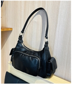 Detail of a black multi-pocket shoulder bag with gold hardware on a wooden background