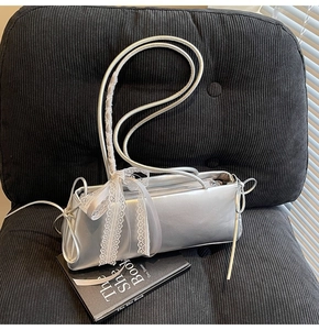 Detail of silver baguette bag with white lace bows and metallic finish on a sofa