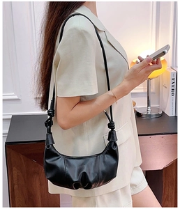 Detail view of a black leather croissant bag with knotted strap worn by a model