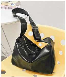 Close-up of minimalist black glossy shoulder bag with silver zipper and wide strap